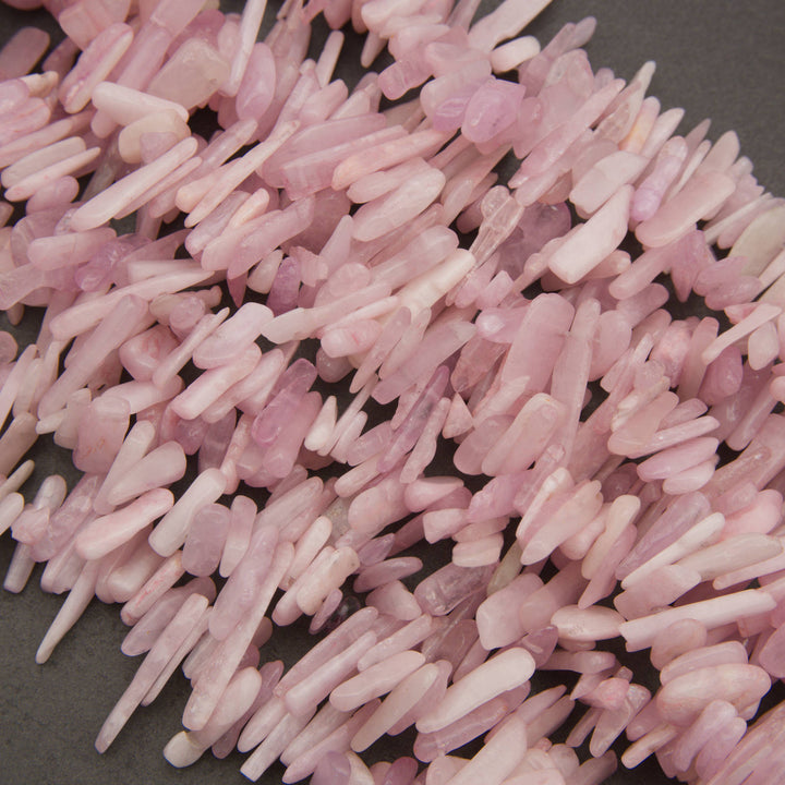 A pile of pale pink polished stone chips or chips with a smooth, matte finish, scattered on a dark gray background.