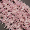 A pile of pale pink polished stone chips or chips with a smooth, matte finish, scattered on a dark gray background.