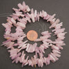 A strand of light pink raw quartz chip beads arranged in a circle on a dark gray background, with a US penny placed in the center for scale.