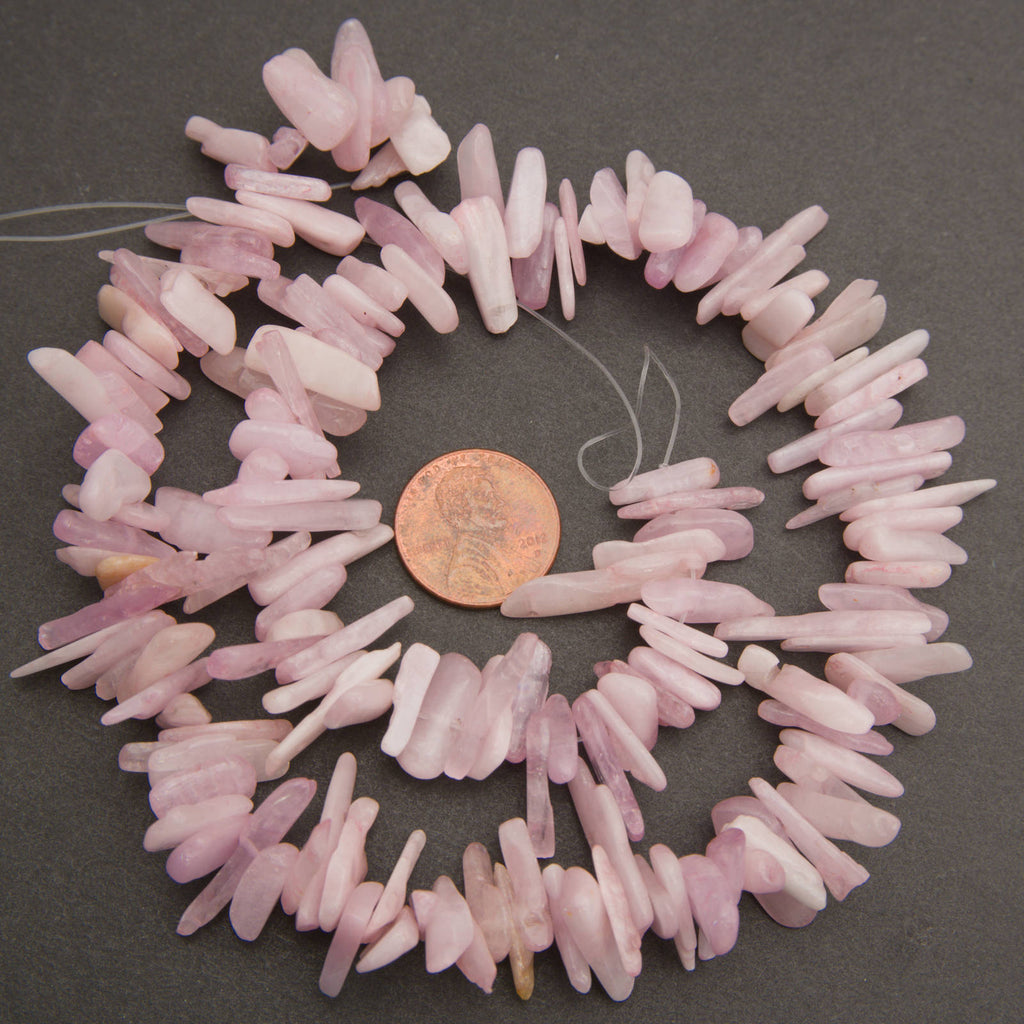 A strand of light pink raw quartz chip beads arranged in a circle on a dark gray background, with a US penny placed in the center for scale.