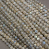 A pile of small, round, polished labradorite gemstone beads with a natural gray and beige base and a subtle iridescent blue flash.