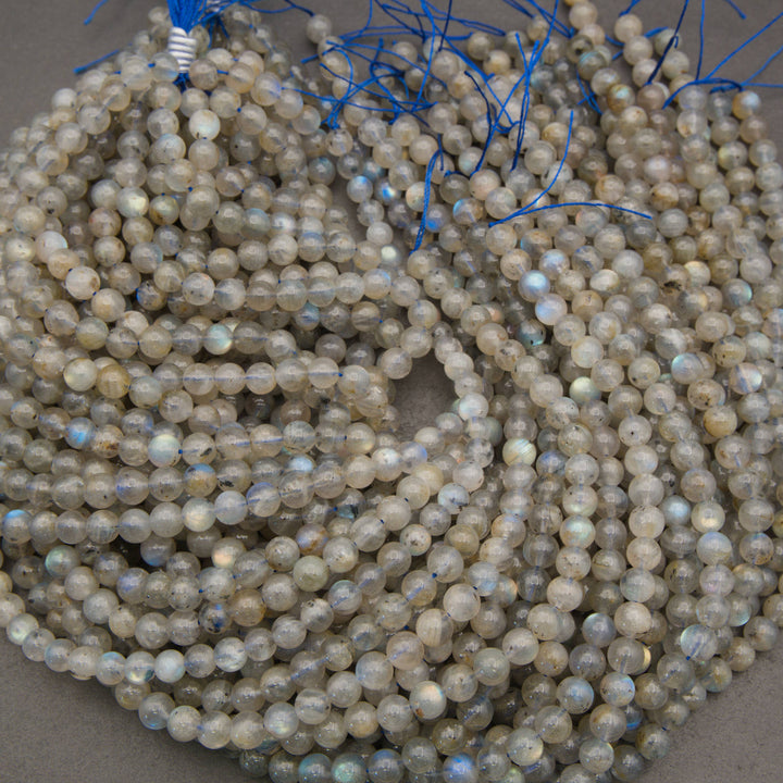 Multiple strands of round labradorite beads with a milky gray base and iridescent blue, green, and gold flashes, coiled together with blue thread ends visible at the top.