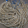 Multiple strands of round labradorite beads with a milky gray base and iridescent blue, green, and gold flashes, coiled together with blue thread ends visible at the top.