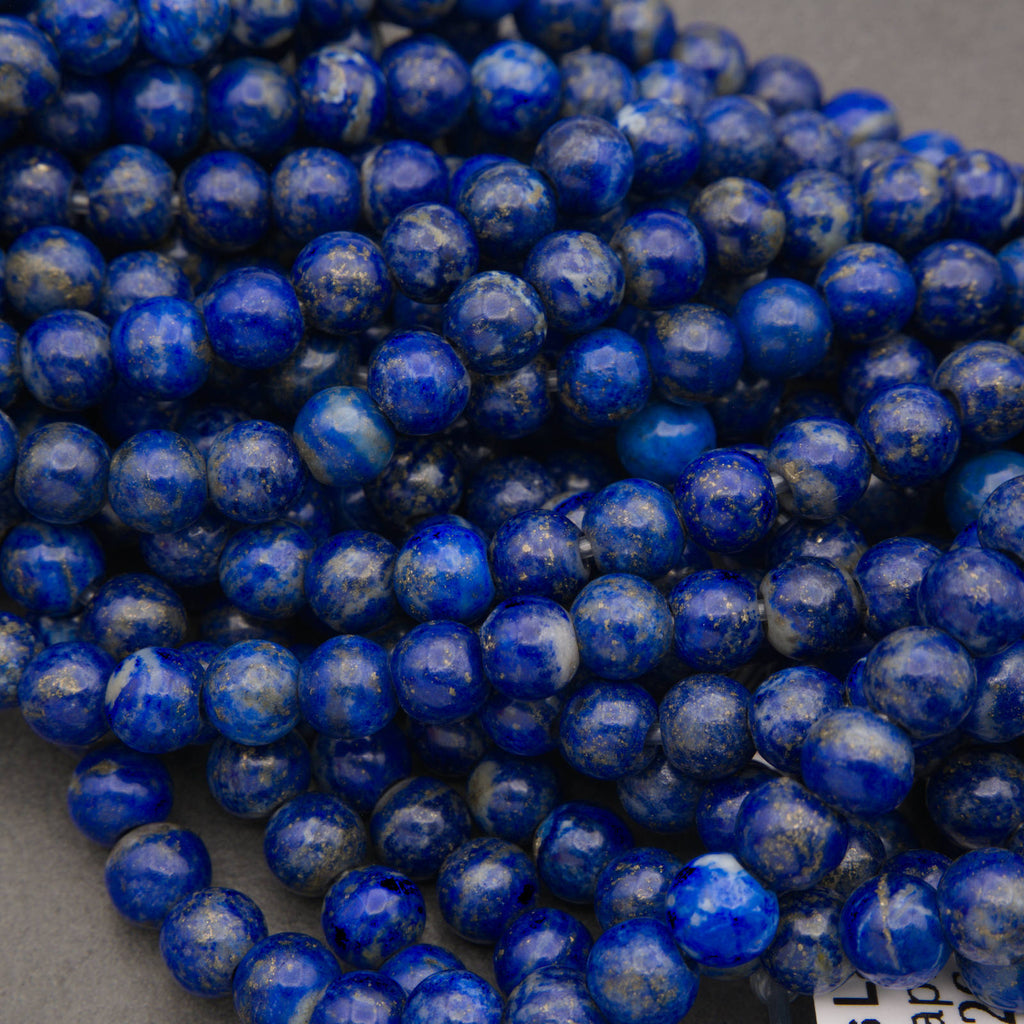 A close-up pile of round, polished lapis lazuli stone beads in deep blue with white cloudy inclusions, resting on a neutral gray surface.