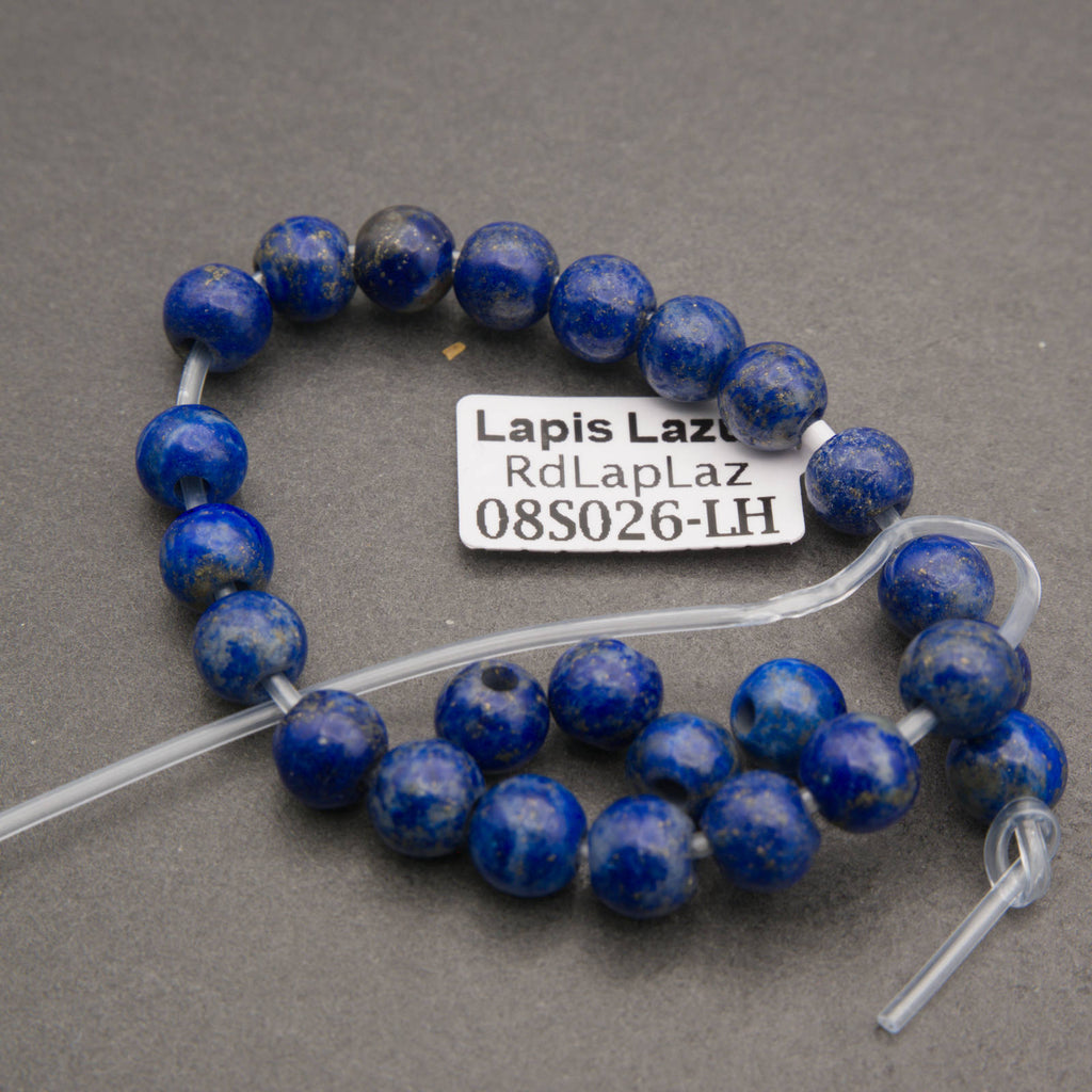 A strand of round lapis lazuli beads on a clear cord, displayed on a gray background with a white label tag that reads 'Lapis Laz RdLapLaz 08S026-LH'.