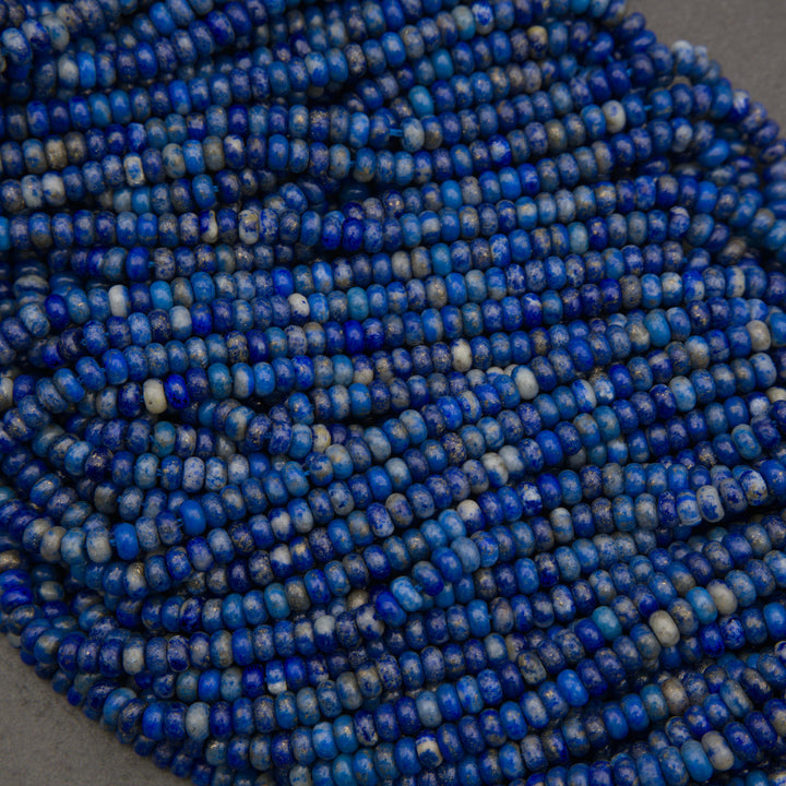 Multiple strands of lapis lazuli rondelle beads showcasing deep ultramarine blue, gray matrix, and golden pyrite inclusions.