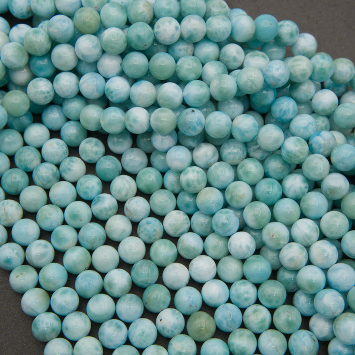 Smooth round larimar bead strands on a gray background in turquoise blue and white