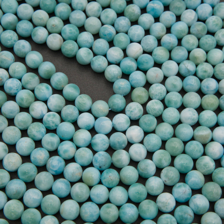 Rows of smooth round larimar beads on a gray background in turquoise blue with white patterns