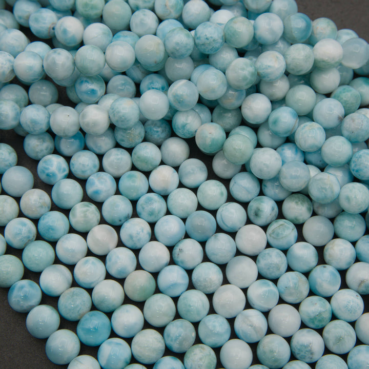 Smooth round larimar bead strands on a gray background in pale blue and white