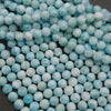 Smooth round larimar bead strands on a gray background in pale blue and white