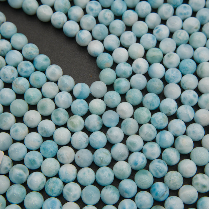 Rows of smooth round larimar beads on a gray background in pale sky blue and white