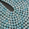 Rows of smooth round larimar beads on a gray background in pale sky blue and white