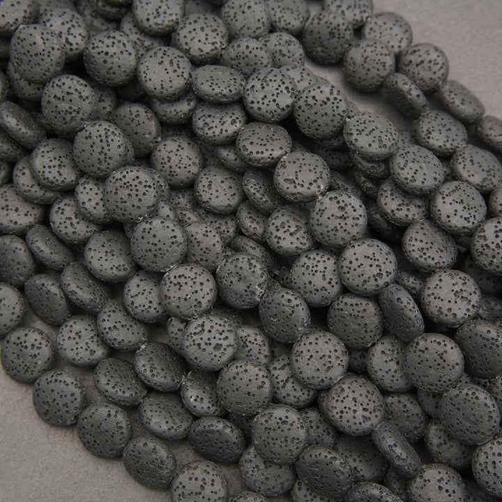 Multiple strands of matte black lava stone coin beads displaying natural pores and deep charcoal-black surfaces.