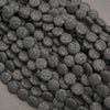 Multiple strands of matte black lava stone coin beads displaying natural pores and deep charcoal-black surfaces.