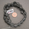 Close-up of black lava rock coin beads featuring rounded, flattened shapes and distinctive volcanic pitting.