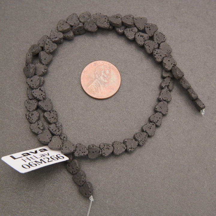 1. Strand of black lava stone heart beads displayed beside a penny for size reference, showing natural volcanic texture.