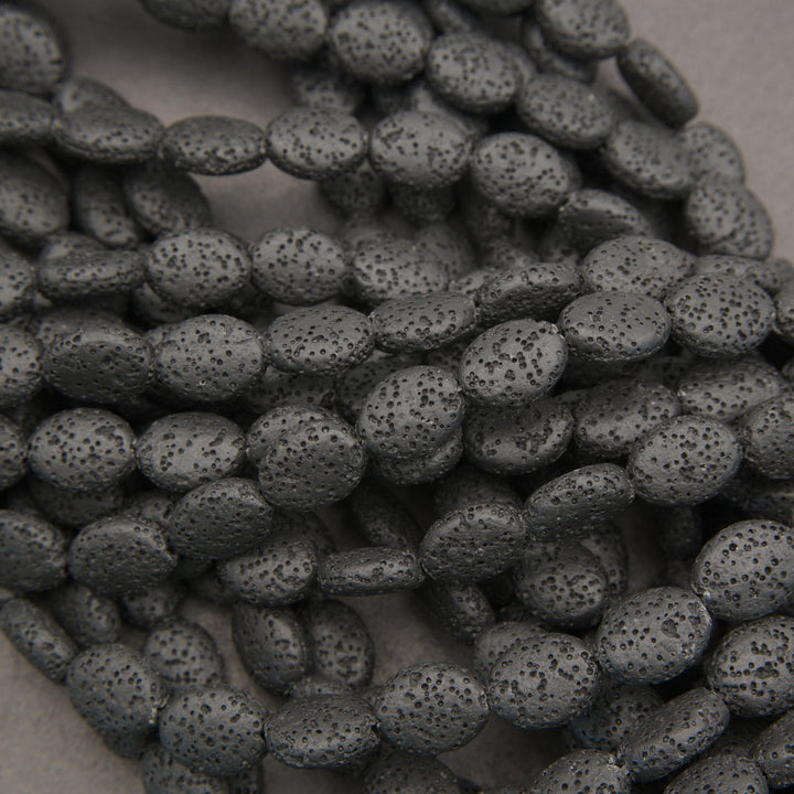 Strands of black volcanic lava stone oval beads with textured surfaces for handmade bracelets and necklaces.