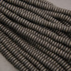 Multiple strands of matte black lava stone disk beads showcasing natural pores and charcoal-black surfaces.