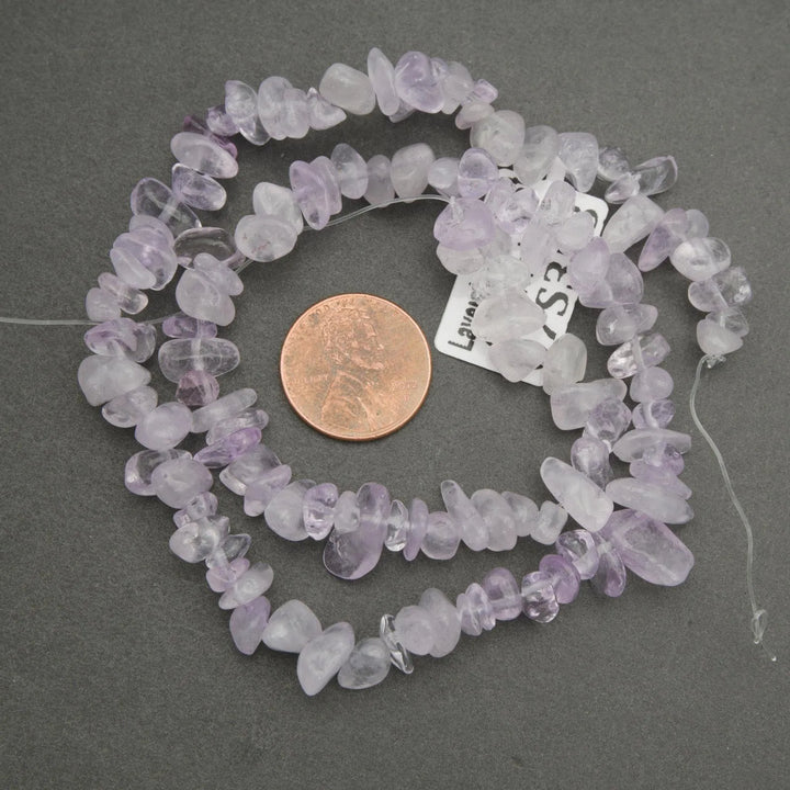 Necklace of lavender amethyst chips with a penny for scale on a gray background