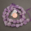 A strand of rough raw lavender amethyst nugget beads coiled around a penny for scale on a gray background
