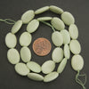 Light green beads on a string with a penny for size comparison on a dark background