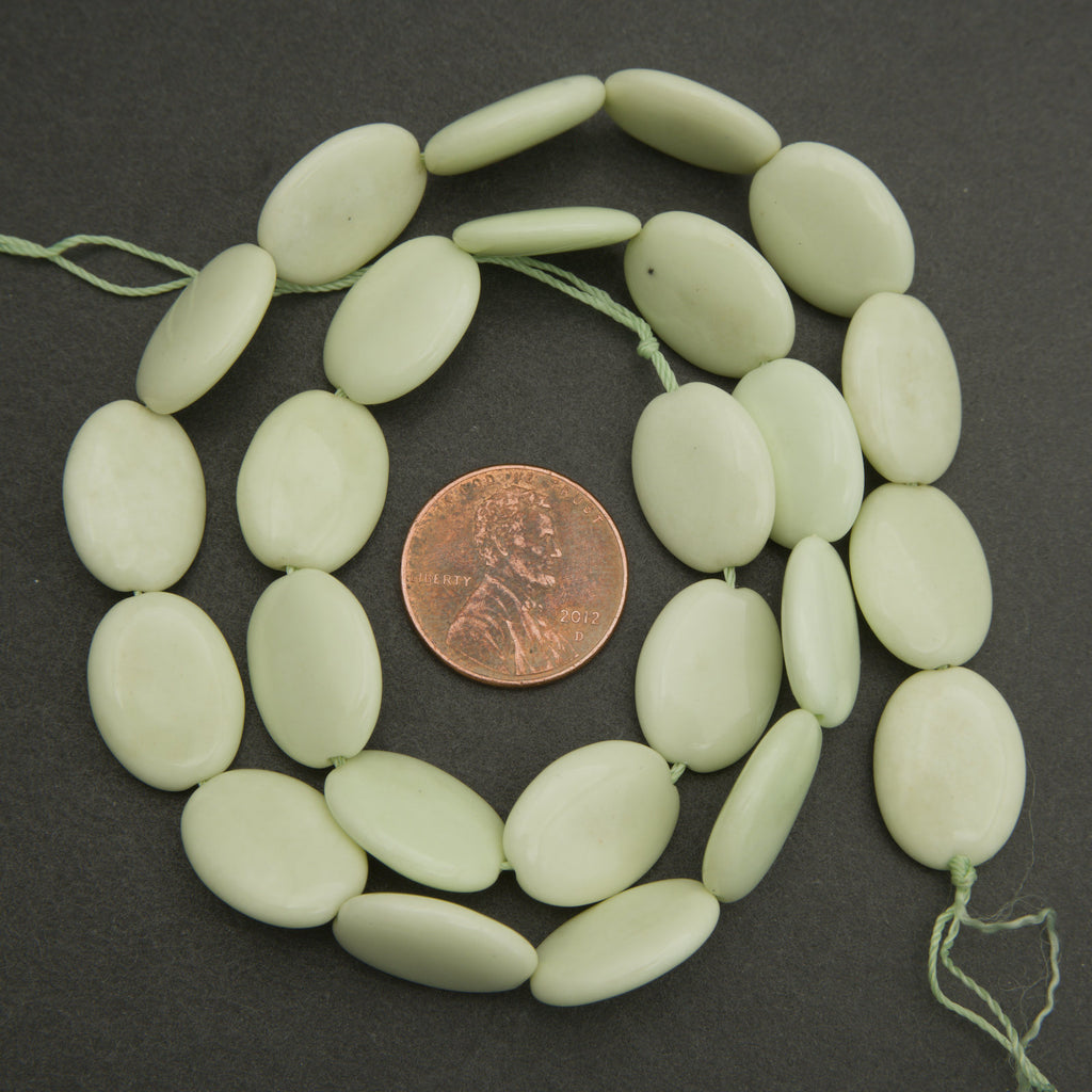 Light green beads on a string with a penny for size comparison on a dark background