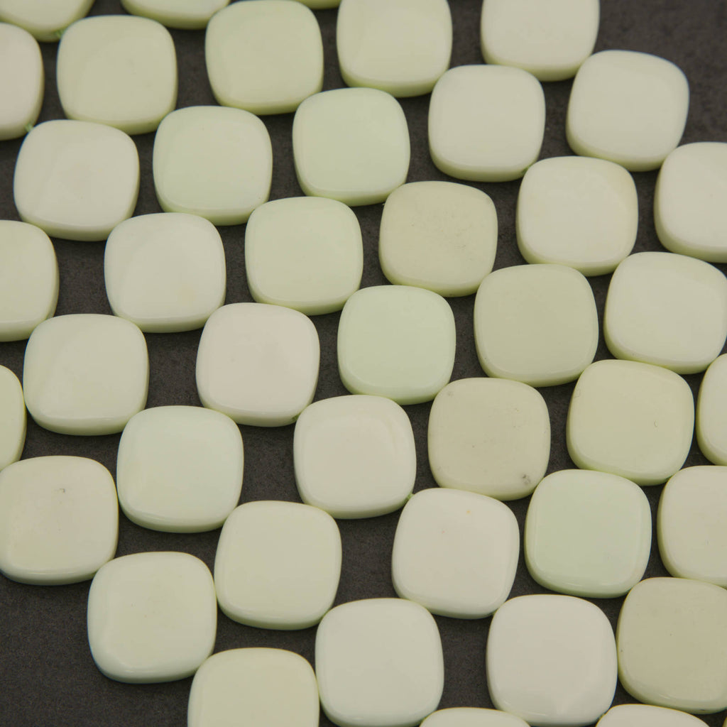 A close-up of many small rounded square tiles in a warm off-white or cream color, arranged on a dark background.
