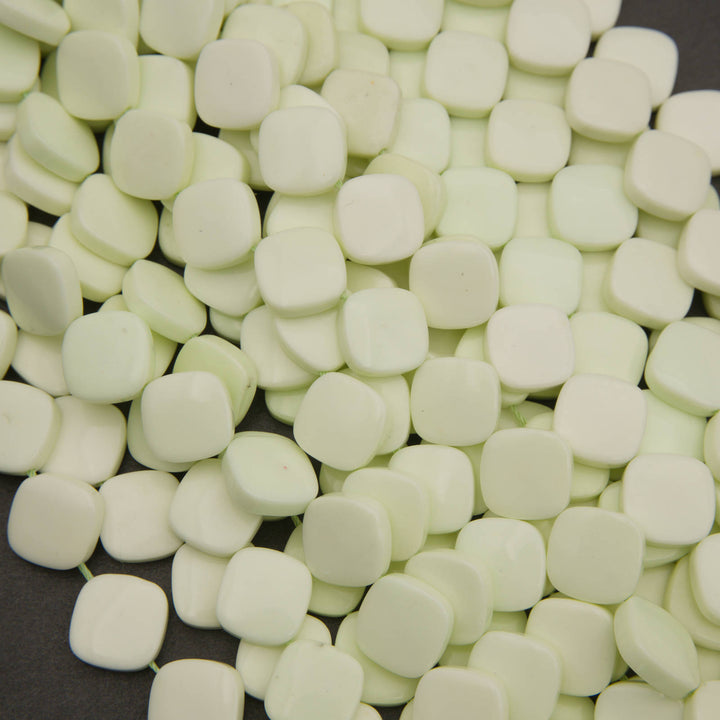 A close-up pile of small, rounded square beads in a pale mint green color, filling almost the entire frame.