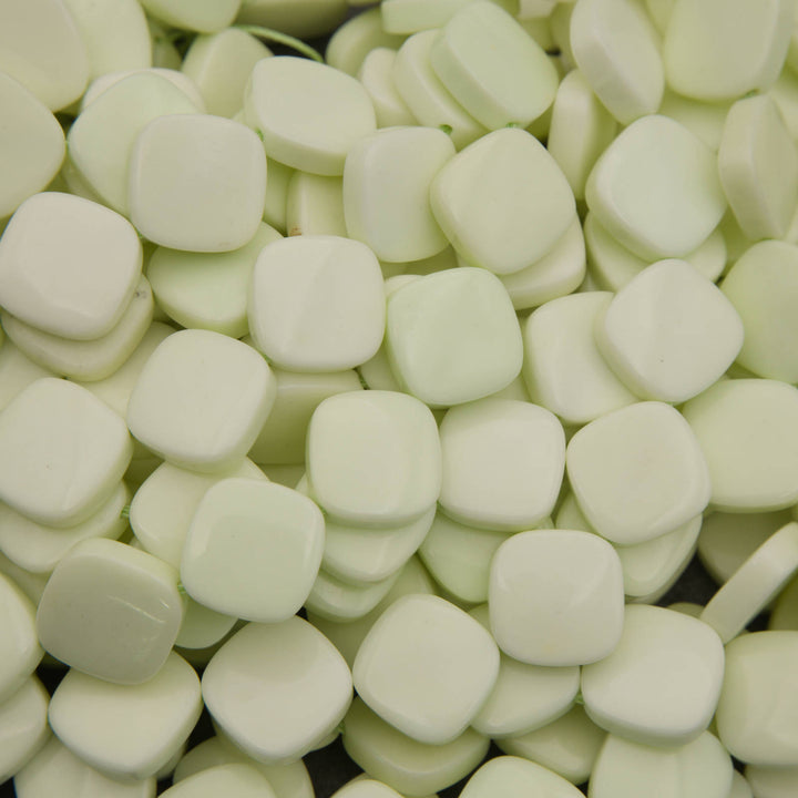 A close-up pile of small, rounded square wax melts in a pale, creamy off-white color.
