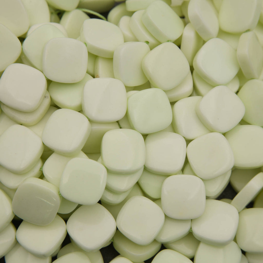 A close-up pile of small, rounded square wax melts in a pale, creamy off-white color.
