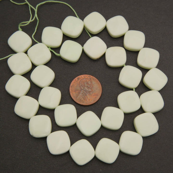 A strand of matte off-white square beads with rounded corners, arranged in a circle on a dark background with a copper coin in the center for scale.