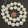 A strand of matte off-white square beads with rounded corners, arranged in a circle on a dark background with a copper coin in the center for scale.