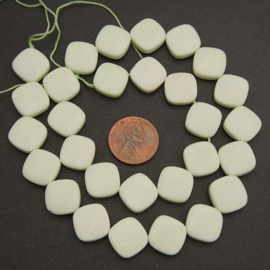 A strand of matte off-white square beads with rounded corners, arranged in a circle on a dark background with a copper coin in the center for scale.