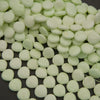 Light green button beads scattered on a dark surface