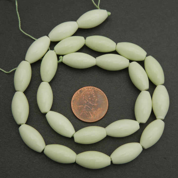 Light green beads on a string with a penny for size comparison on a dark background