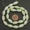Light green beads on a string with a penny for size comparison on a dark background