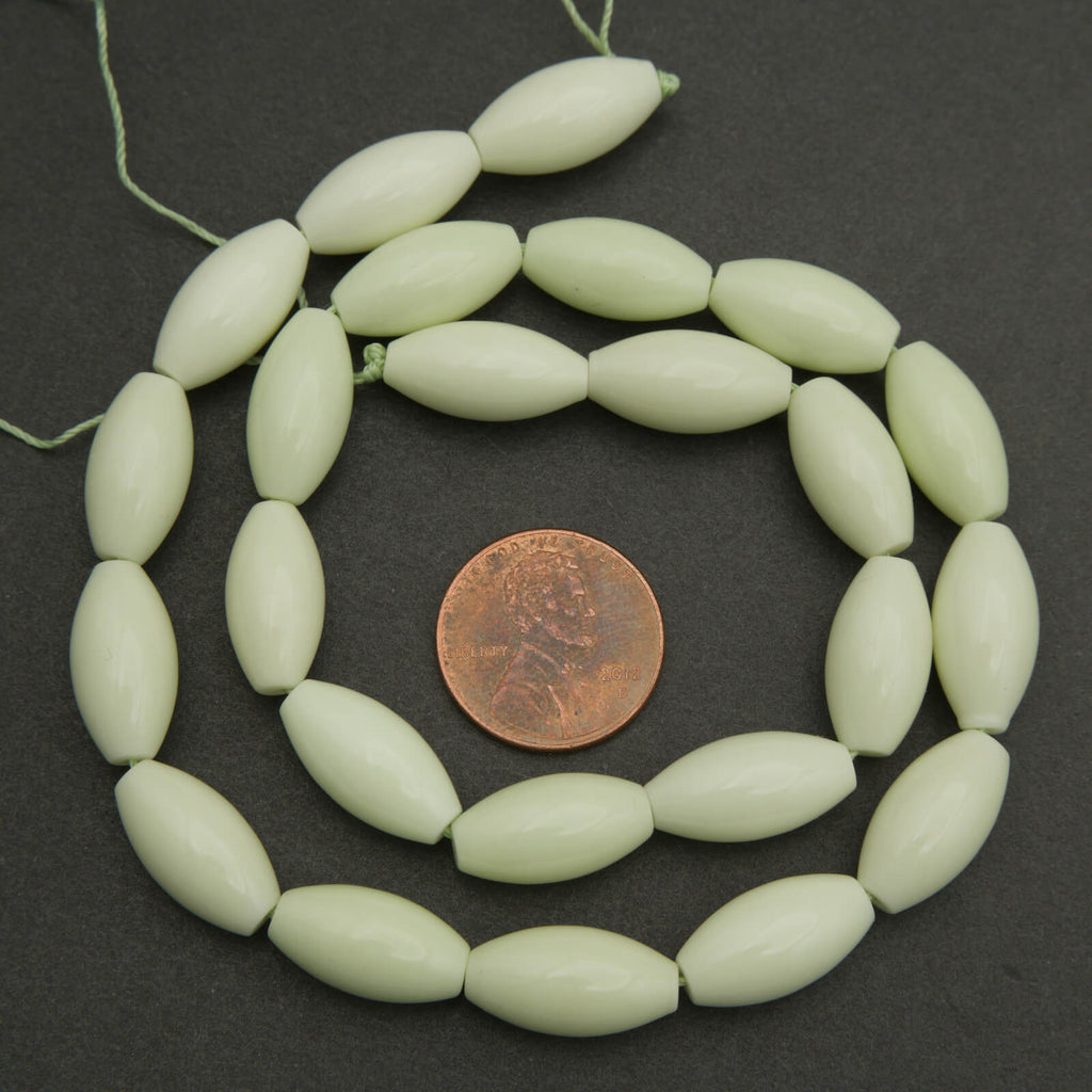 Light green beads on a string with a penny for size comparison on a dark background
