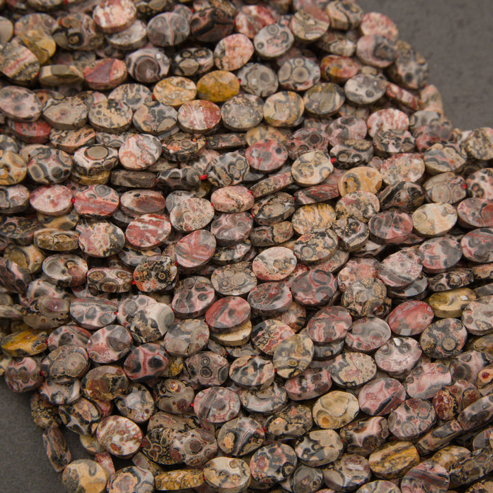 Rows of faceted leopard skin jasper oval beads on a gray background with charcoal spots and rings
