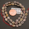 A strand of faceted leopard skin jasper oval beads coiled around a penny for scale
