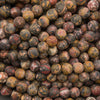 A close-up pile of round, mottled beads in earthy tones, including brown, beige, red, and black, filling the entire frame.