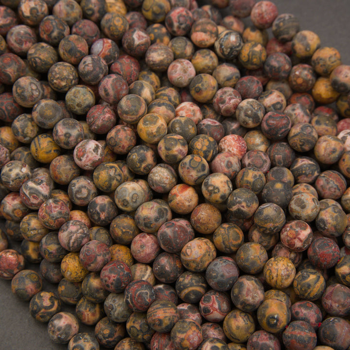 A close-up pile of round stone beads with mottled earthy patterns in brown, gray, red, yellow, and black.