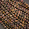 A close-up pile of round stone beads with mottled earthy patterns in brown, gray, red, yellow, and black.