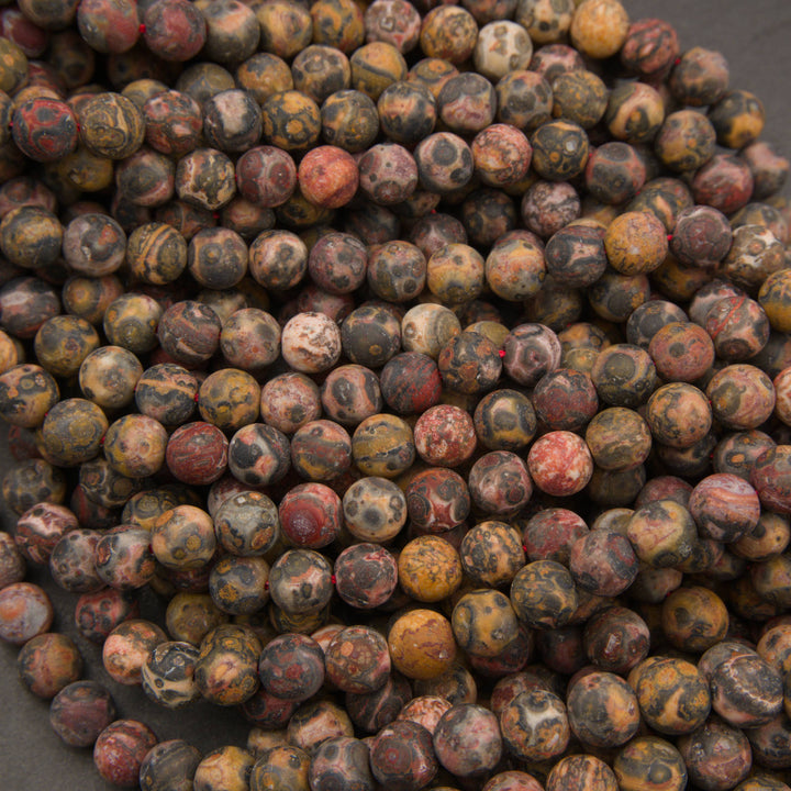 A pile of round cabochon gemstone beads featuring a marbled pattern of red, yellow, brown, and black.