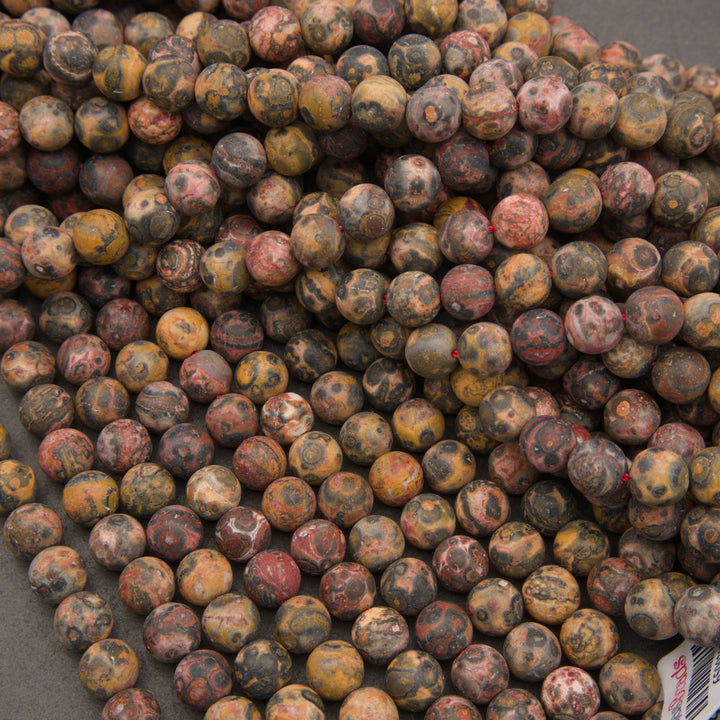 A pile of round gemstone beads with a mottled, marbled pattern in earthy tones of brown, yellow, red, and gray.