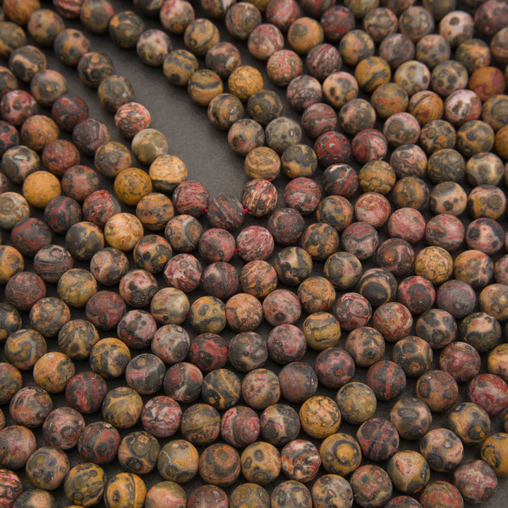 Close-up of many round stone beads in earthy marbled colors, including brown, gray, red, and tan, arranged on a dark surface.