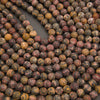 Close-up of many round stone beads in earthy marbled colors, including brown, gray, red, and tan, arranged on a dark surface.
