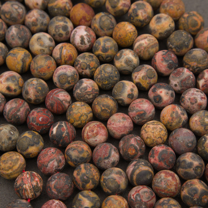 A close-up pile of round gemstone beads with mottled patterns of red, brown, black, and yellow.