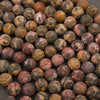 A close-up pile of round gemstone beads with mottled patterns of red, brown, black, and yellow.