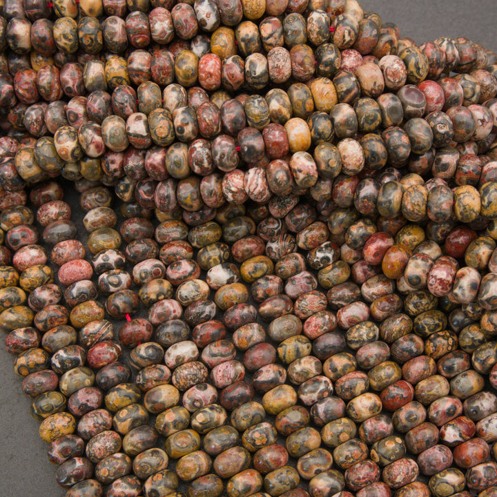 A close-up pile of polished oval beads with a mottled, marbled pattern in earthy tones of brown, beige, red, and gray.