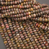 A close-up pile of polished oval beads with a mottled, marbled pattern in earthy tones of brown, beige, red, and gray.